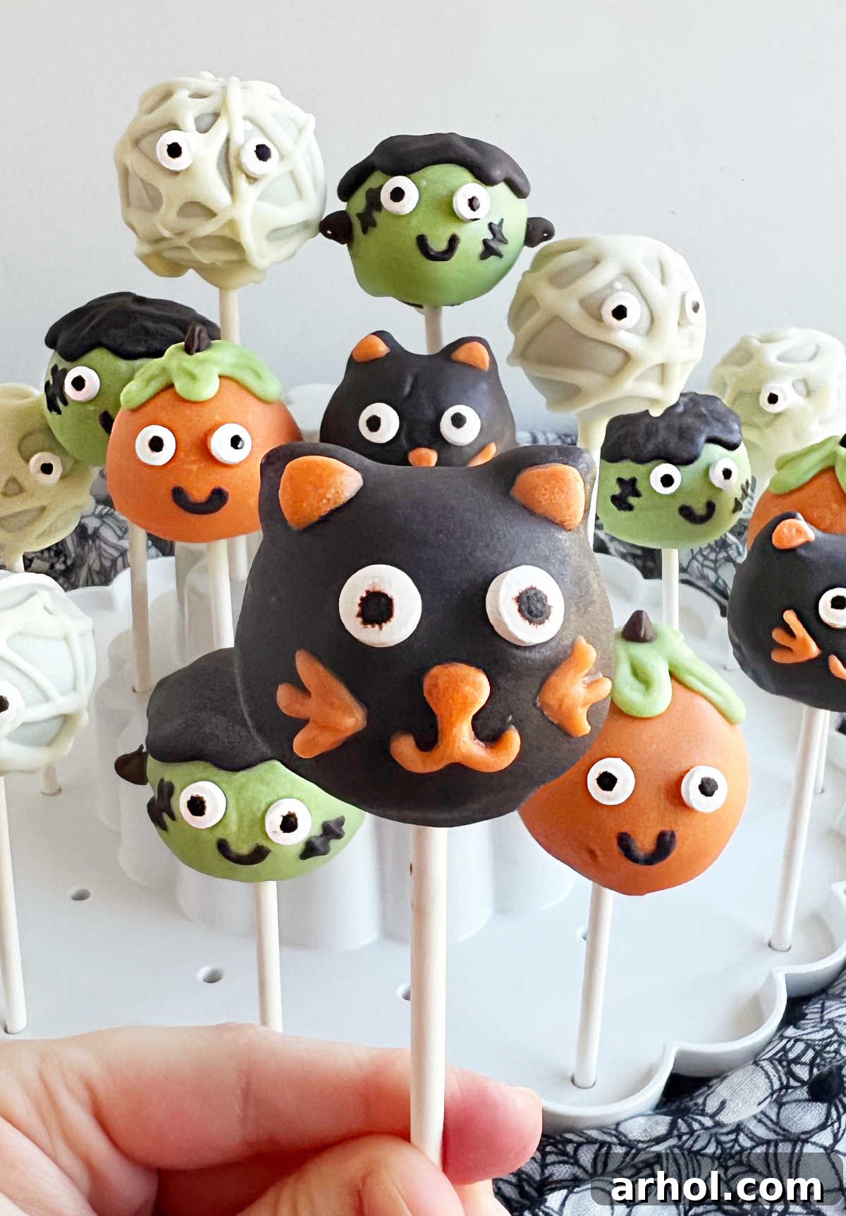 A hand gently holding a decorated black cat cake pop, showcased on its stick, ready to be enjoyed.