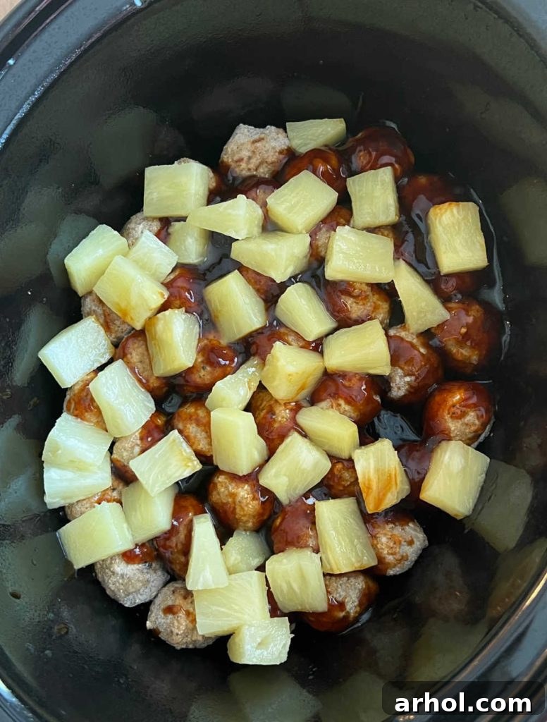 Frozen meatballs and pineapple chunks layered in a slow cooker, ready for cooking.