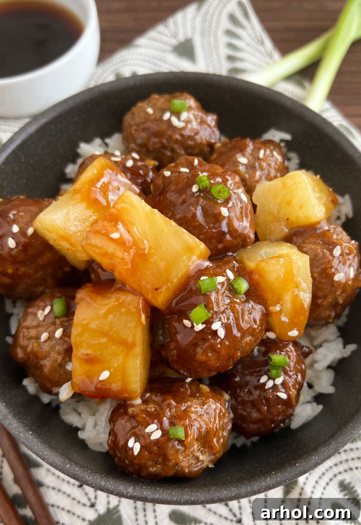 Teriyaki meatballs with pineapple served over a bed of jasmine rice in a bowl, garnished with green onions.