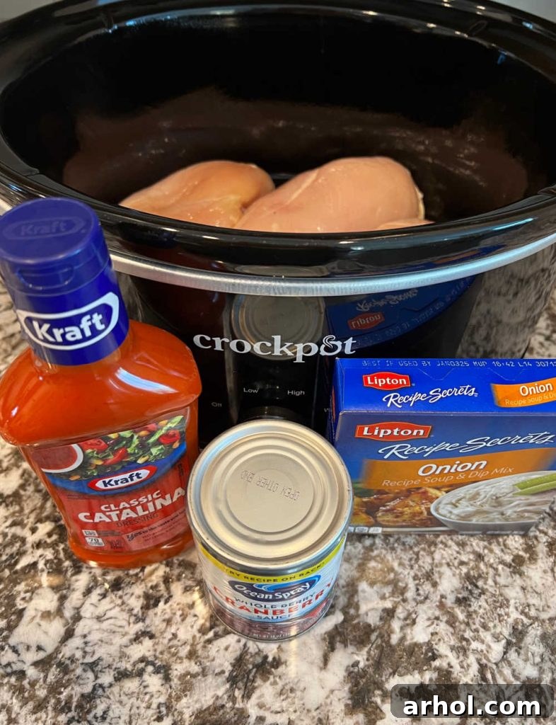 Four key ingredients laid out: boneless chicken breasts, a box of dry onion soup mix, a can of whole berry cranberry sauce, and a bottle of Catalina salad dressing.