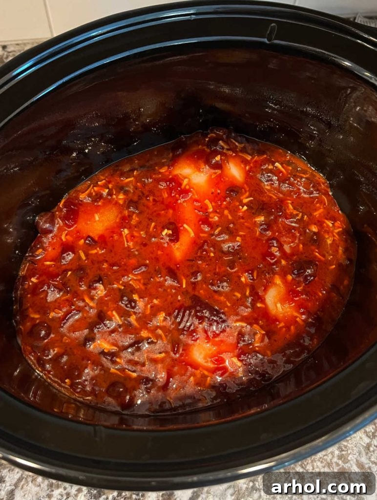 Boneless chicken breasts are completely covered in the cranberry sauce mixture within the slow cooker, ready for cooking.