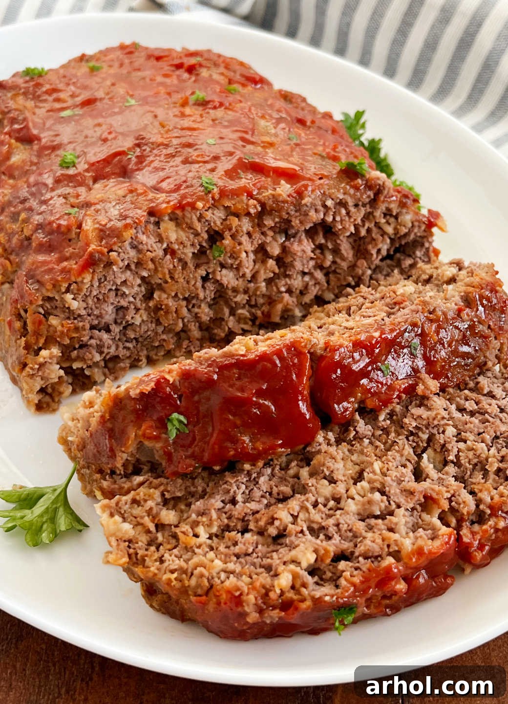 Slices of Quaker Oats meatloaf with a rich ketchup glaze, served on a white platter and garnished with fresh parsley.