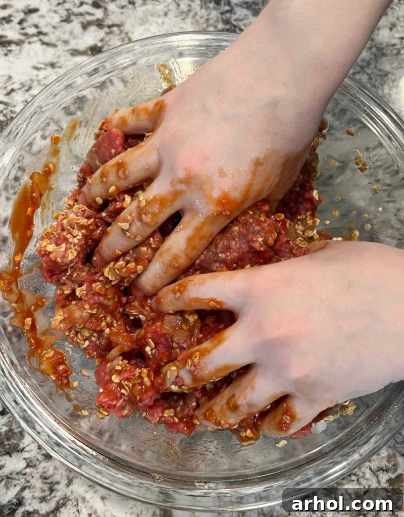 Hands gently mixing ground beef and other meatloaf ingredients in a large bowl, ensuring even distribution.