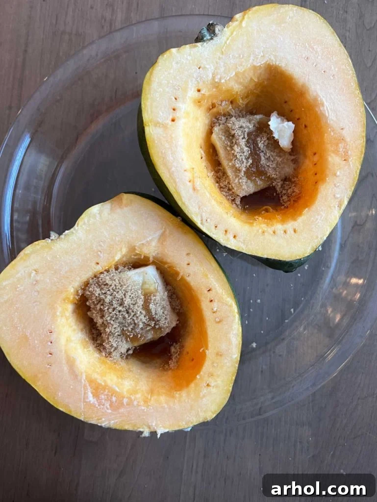 Two acorn squash halves with butter and brown sugar in the center on a baking dish, ready for the microwave.