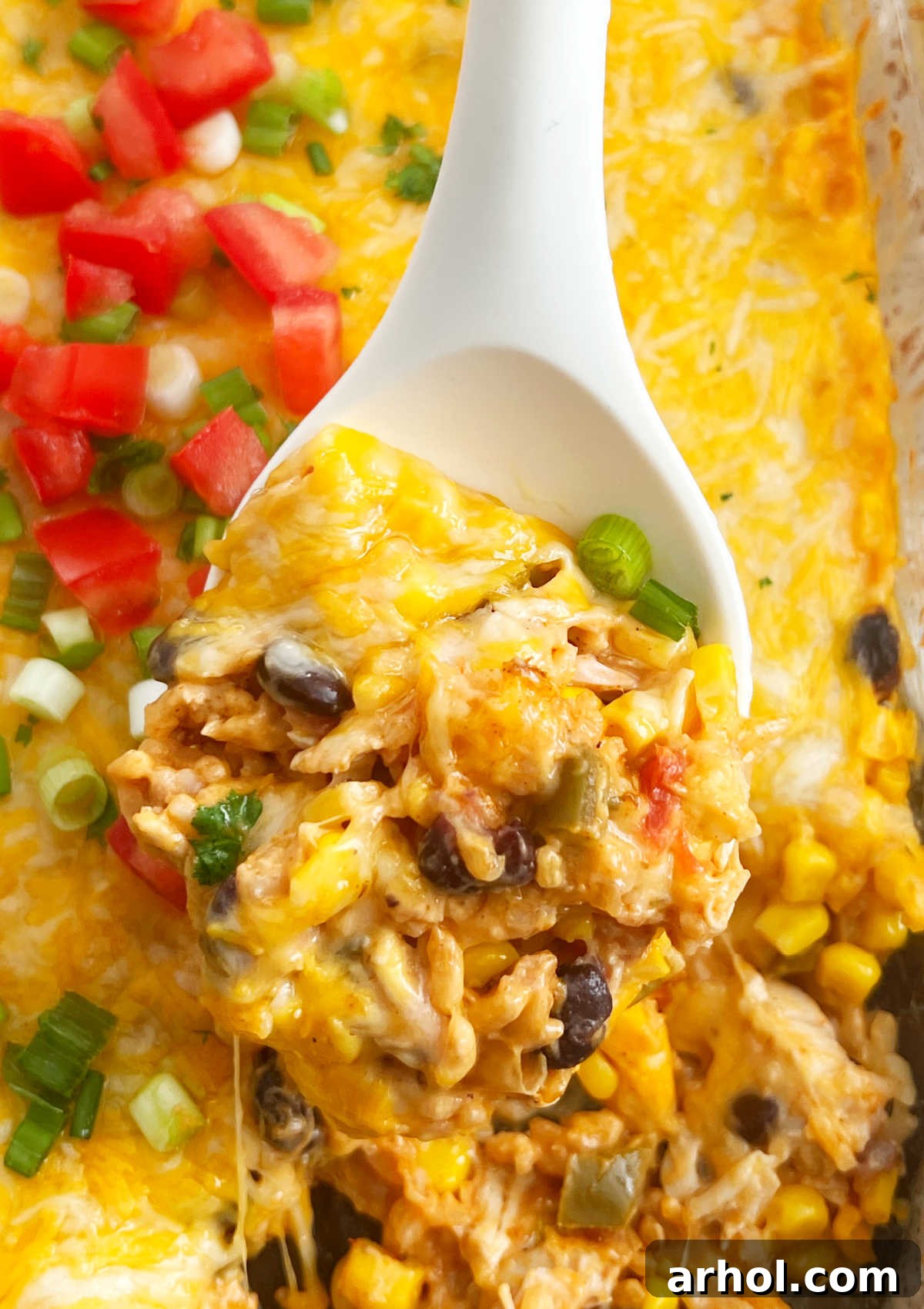 A serving spoon lifting a portion of cheesy Fiesta Chicken Casserole with visible rice, black beans, and corn.