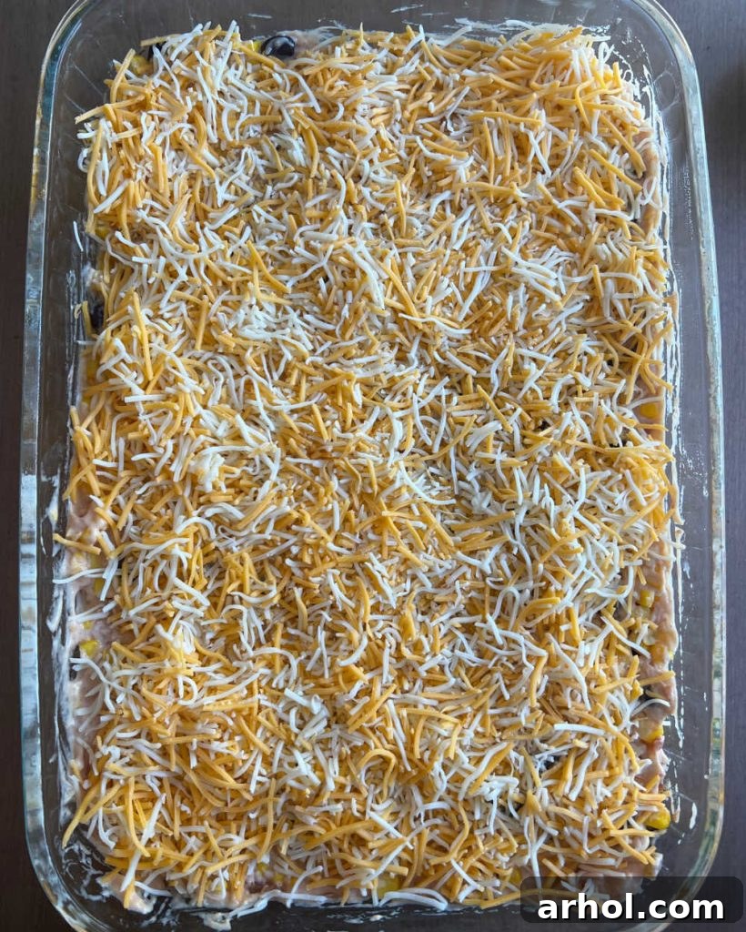 Fiesta Chicken Casserole in a baking dish, topped with shredded cheese, ready for the oven.