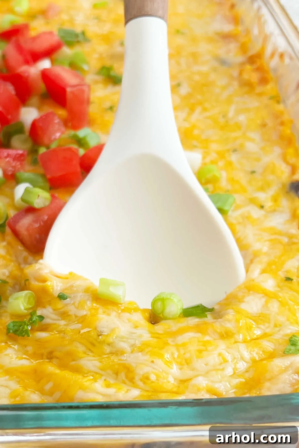 A serving spoon dishing out a portion of hot, cheesy Fiesta Chicken Casserole, fresh from the oven.