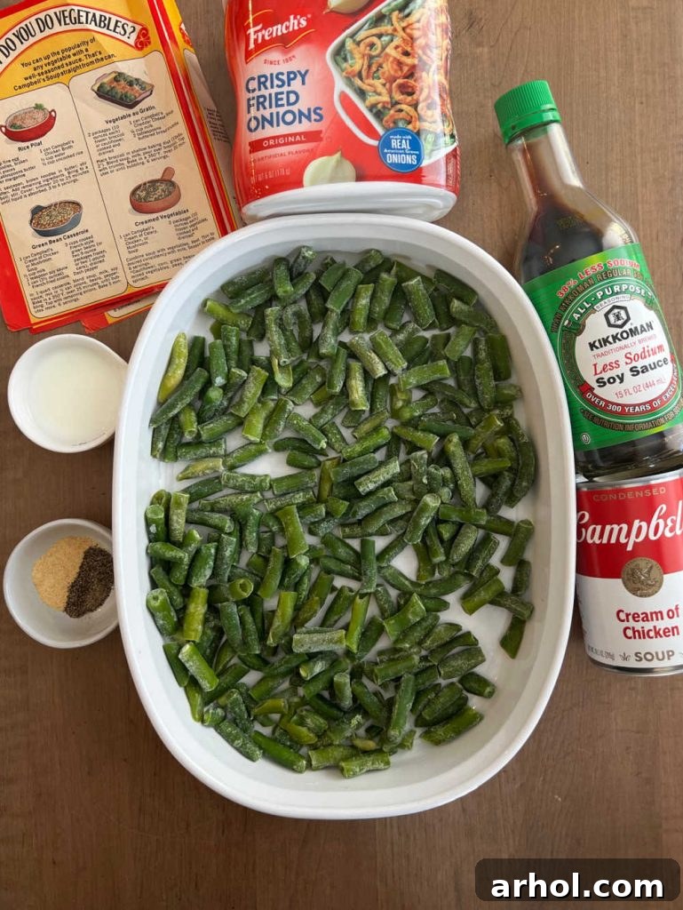 All the key ingredients for green bean casserole laid out: a can of cream of chicken soup, a carton of milk, a bottle of soy sauce, a bag of French's fried onions, fresh green beans, and a pepper grinder.