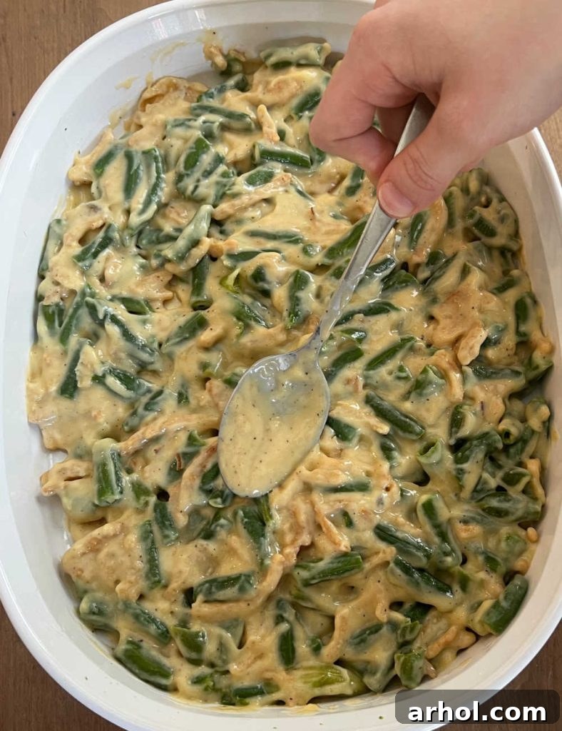 The green bean casserole mixture is spread evenly into a prepared baking dish with a spoon, ready for the oven.