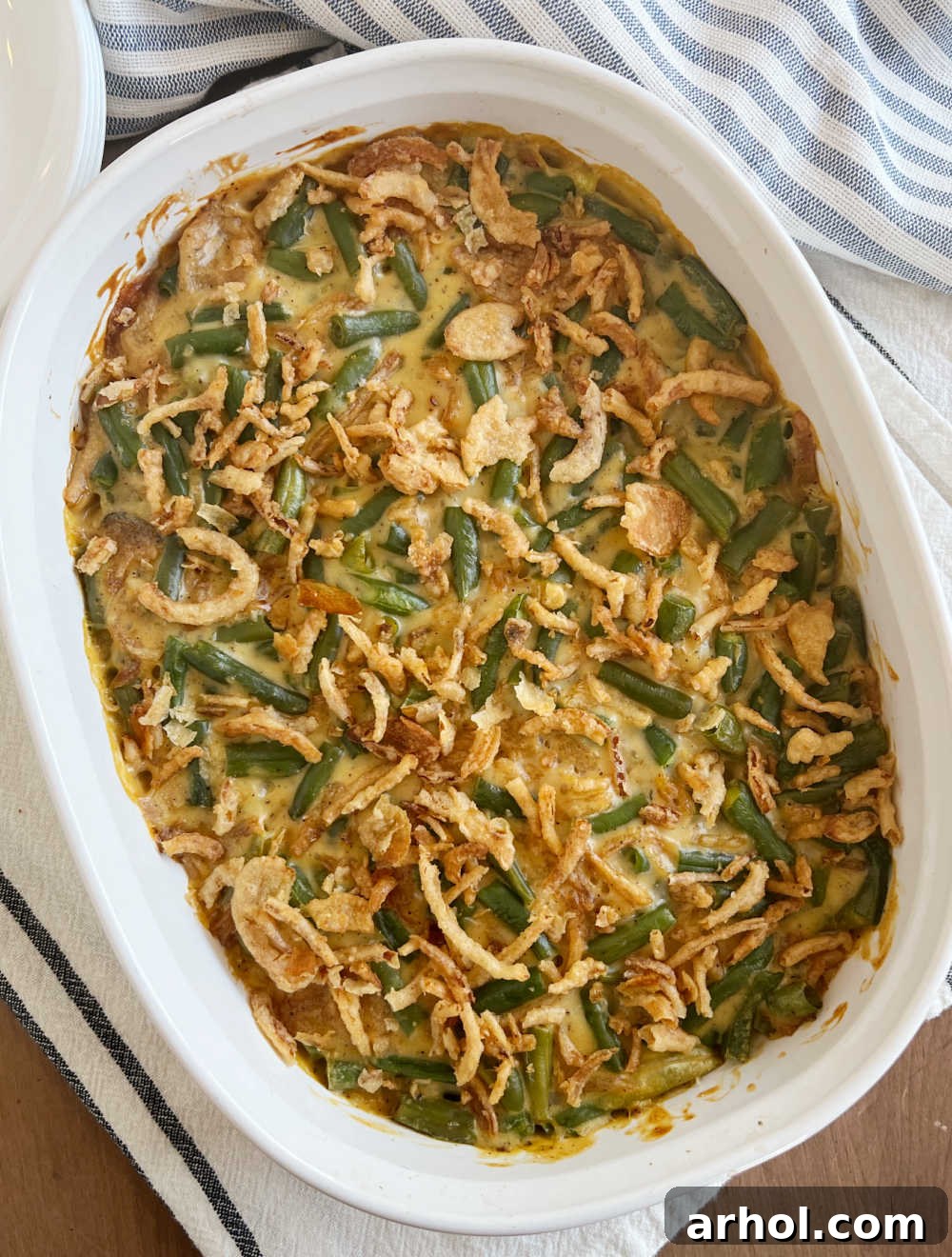 A freshly baked green bean casserole with a golden-brown crispy fried onion topping, served hot in a baking dish on a rustic wooden table, ready to be enjoyed.