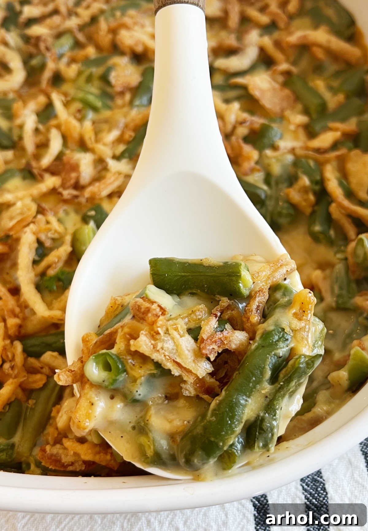 A close-up shot of a single serving of Campbell's green bean casserole on a white serving spoon, showcasing its creamy texture, tender green beans, and crispy onion topping.