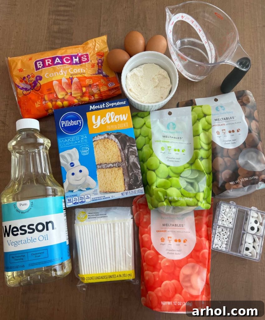 Ingredients laid out: cake mix, frosting, eggs, oil, water, various candy melts, candy corn, candy eyes, and lollipop sticks.