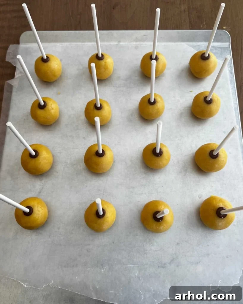 Vanilla cake balls with lollipop sticks inserted, neatly arranged on a wax paper-lined baking sheet, ready for chilling.