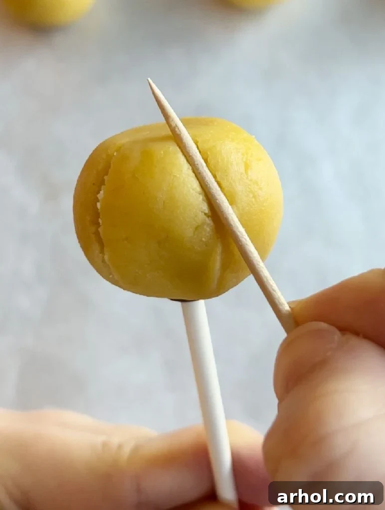 A toothpick being gently pressed into the side of a cake ball to create realistic pumpkin grooves.