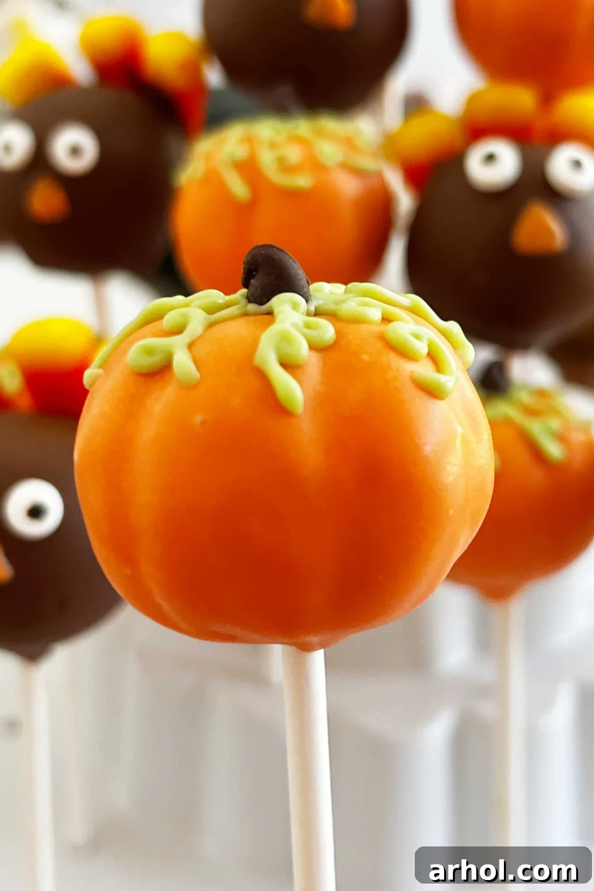 A festive pumpkin cake pop showcasing its vibrant orange coating, a green piped vine, and a mini chocolate chip stem.