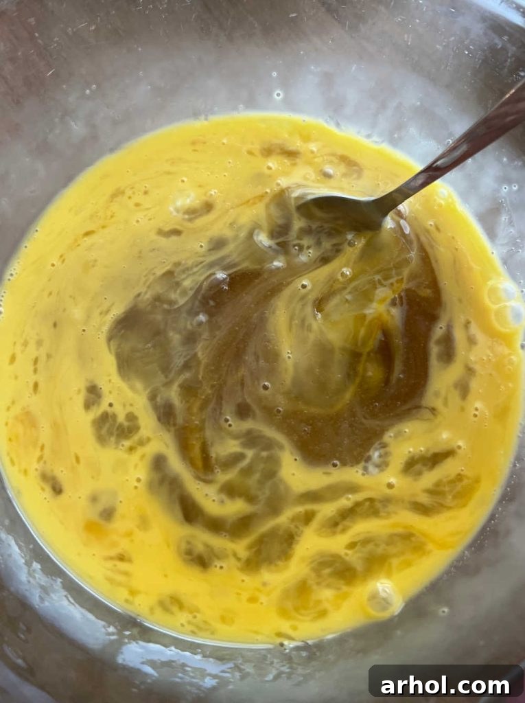 A vibrant view of the liquid ingredients for pecan pie filling: eggs, corn syrup, melted butter, sugars, vanilla, and bourbon, being expertly whisked in a glass mixing bowl until perfectly blended.