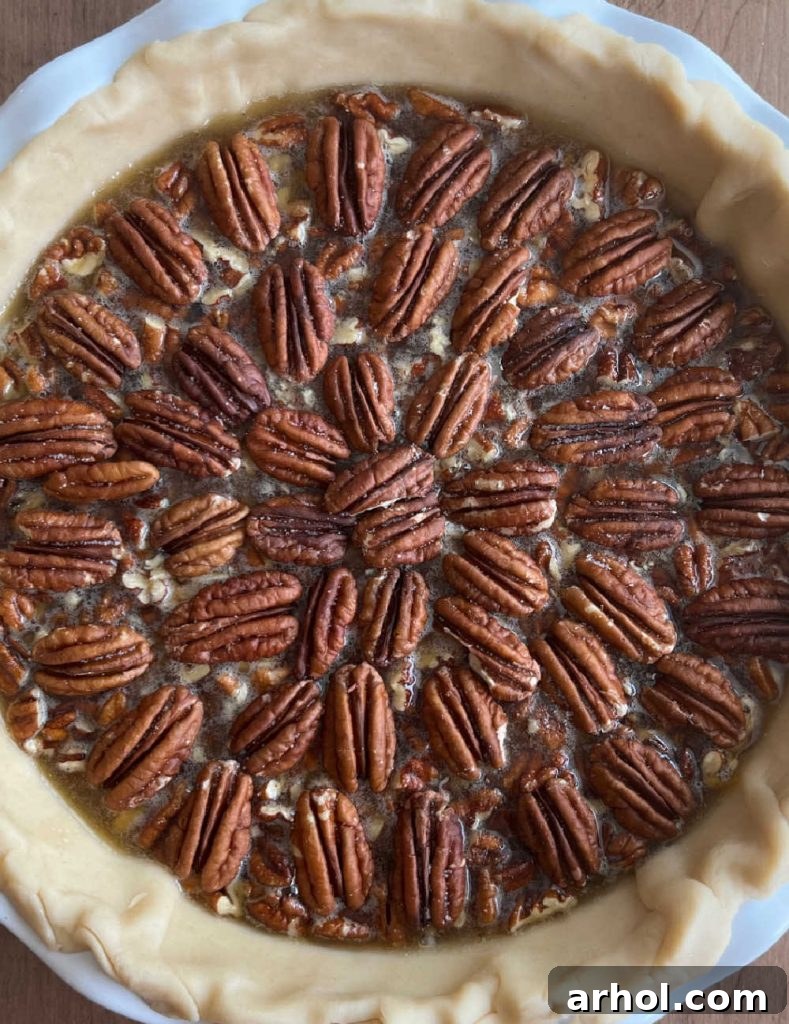 A close-up of whole pecan halves meticulously arranged in a beautiful, decorative pattern on top of an unbaked bourbon chocolate pecan pie filling.