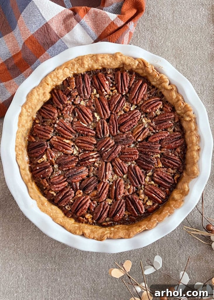 A freshly baked Bourbon Chocolate Pecan Pie, glistening and golden, presented in a clean white pie dish on a light wooden surface.