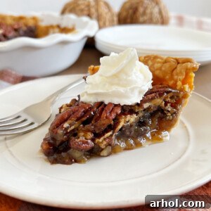 A perfectly portioned slice of Grandma's Bourbon Chocolate Pecan Pie, featuring its rich, glistening filling, crunchy pecan and chocolate layers, and a delicate dollop of whipped cream on top.