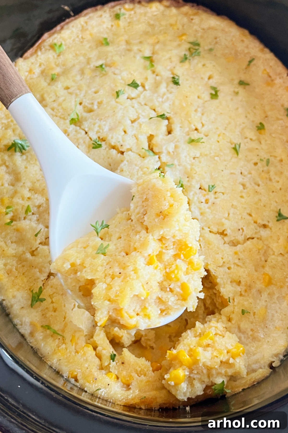 Creamy Crockpot Corn Casserole made with Jiffy Mix, served on a white serving spoon, ready for a holiday meal.