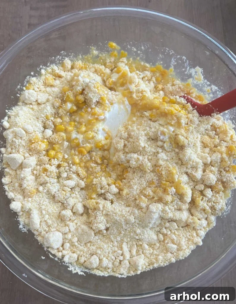 Stirring corn casserole ingredients in a large white mixing bowl for Crockpot Corn Casserole.