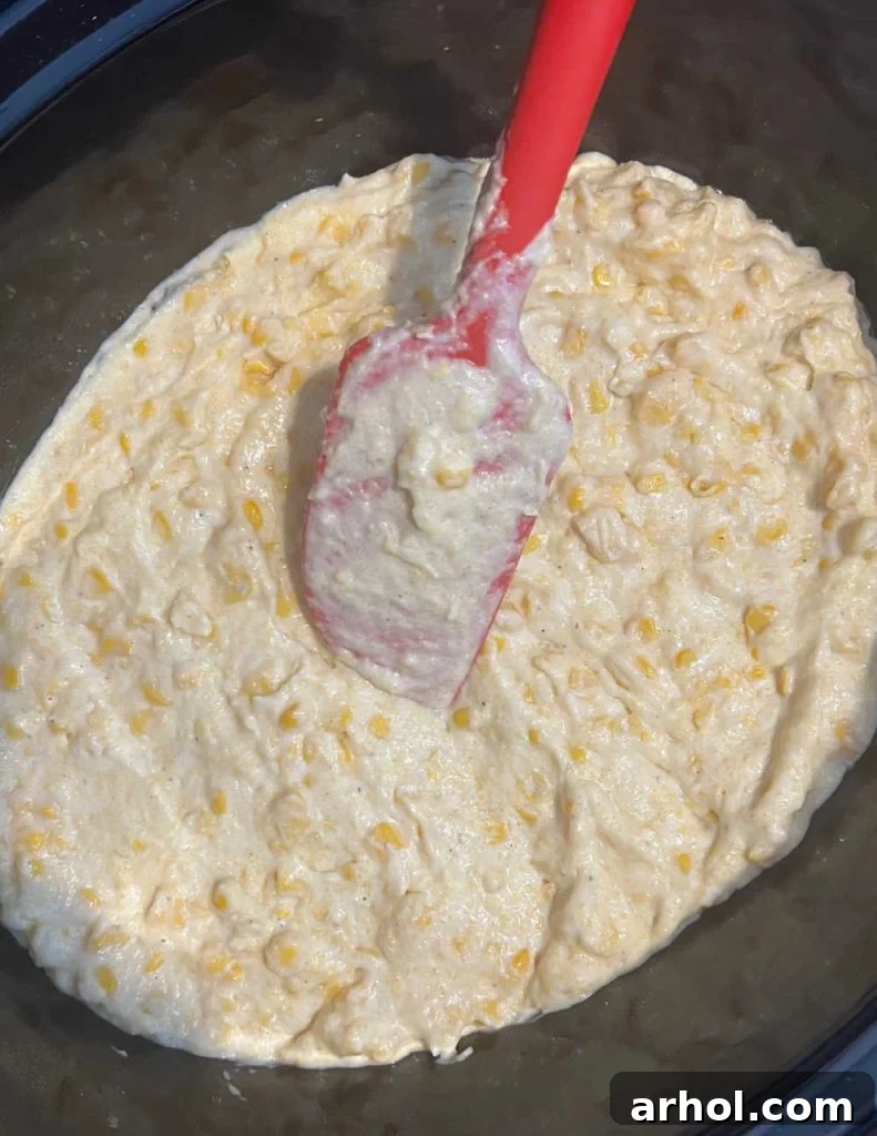 Spreading creamy Jiffy corn casserole mixture evenly into a slow cooker before cooking.
