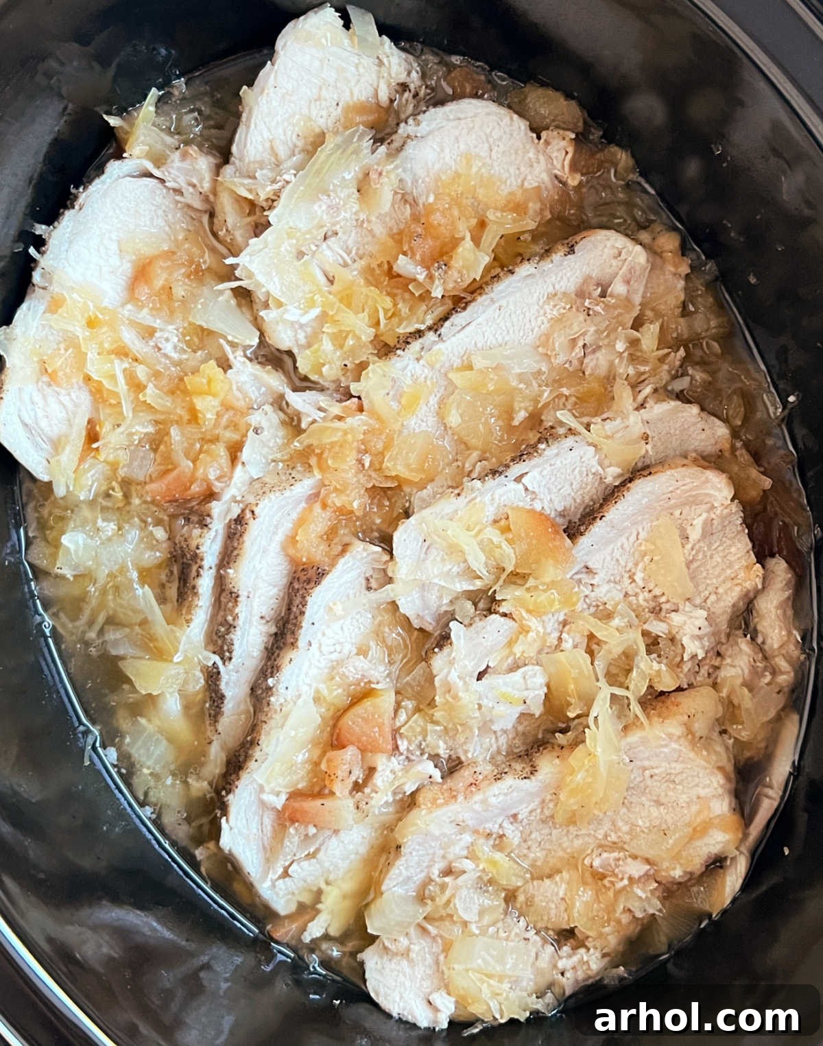 Hearty slow cooker pork roast and sauerkraut in a crock pot, garnished with fresh apple slices and herbs.