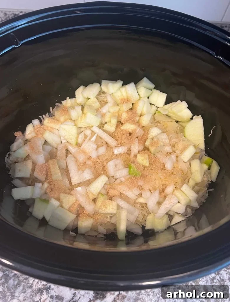 Layer of sauerkraut, apples, and brown sugar prepared in the bottom of a crock pot.