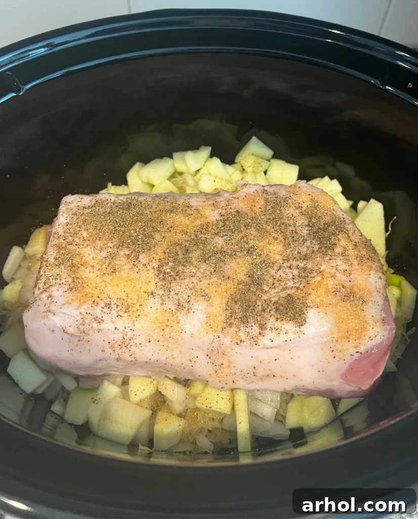 Pork loin roast placed over apples and sauerkraut in a crockpot, ready for slow cooking.