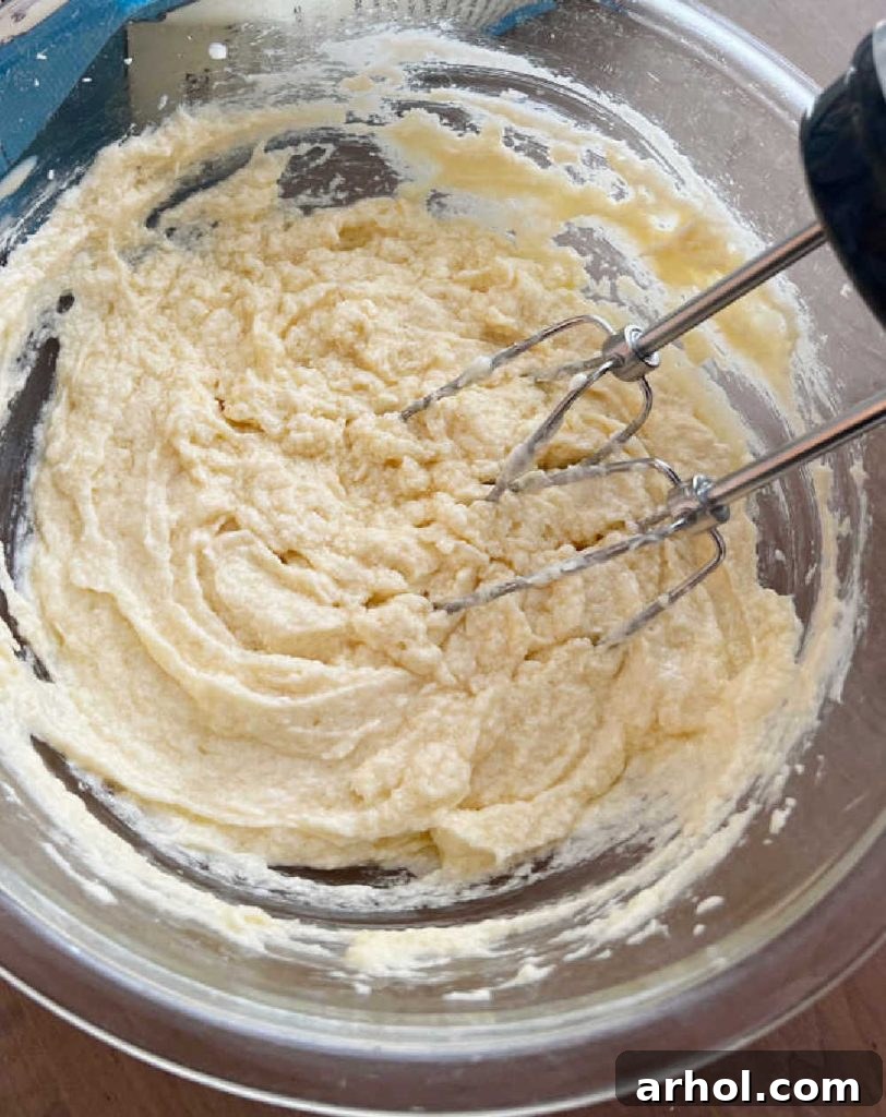 A mixing bowl with cookie dough being prepared using an electric mixer.