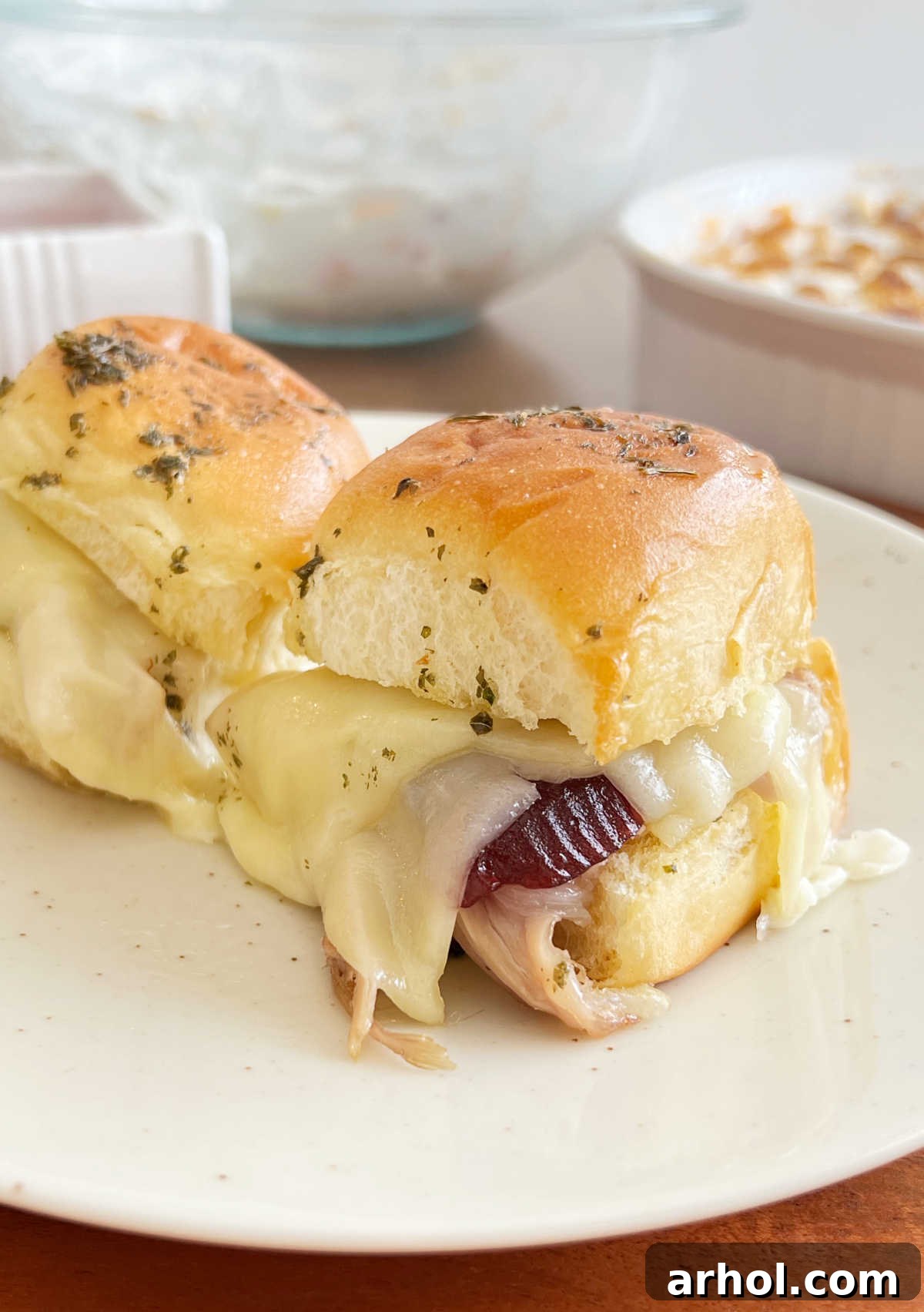 Aloha Turkey Sliders 2 turkey sliders on Hawaiian rolls with cranberry sauce and provolone cheese on plate, ready to be enjoyed.