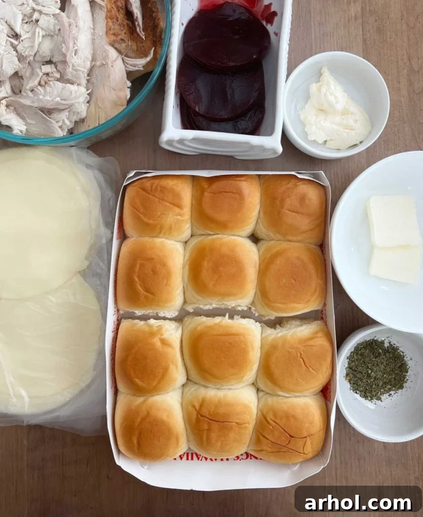 Aloha Turkey Sliders 3 Ingredients for turkey sliders: Hawaiian rolls, provolone cheese, leftover turkey, cranberry sauce, mayonnaise, butter, and dried Italian seasoning laid out on a table.