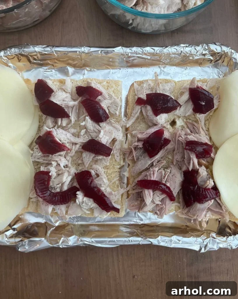 Aloha Turkey Sliders 5 The bottom half of Hawaiian rolls on a baking sheet, layered with mayonnaise, turkey, cranberry sauce, and topped with provolone cheese slices, ready for the top bun.