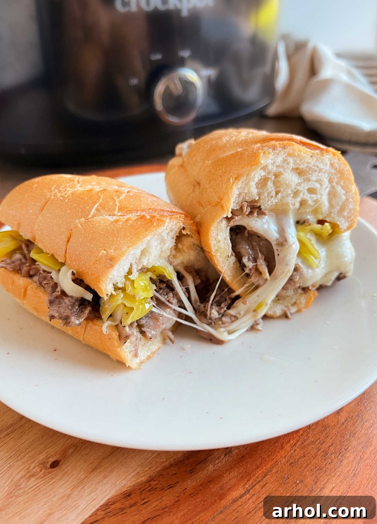 crock pot Italian beef sandwiches sliced in half with melted provolone cheese, showcasing a delicious, ready-to-eat meal.