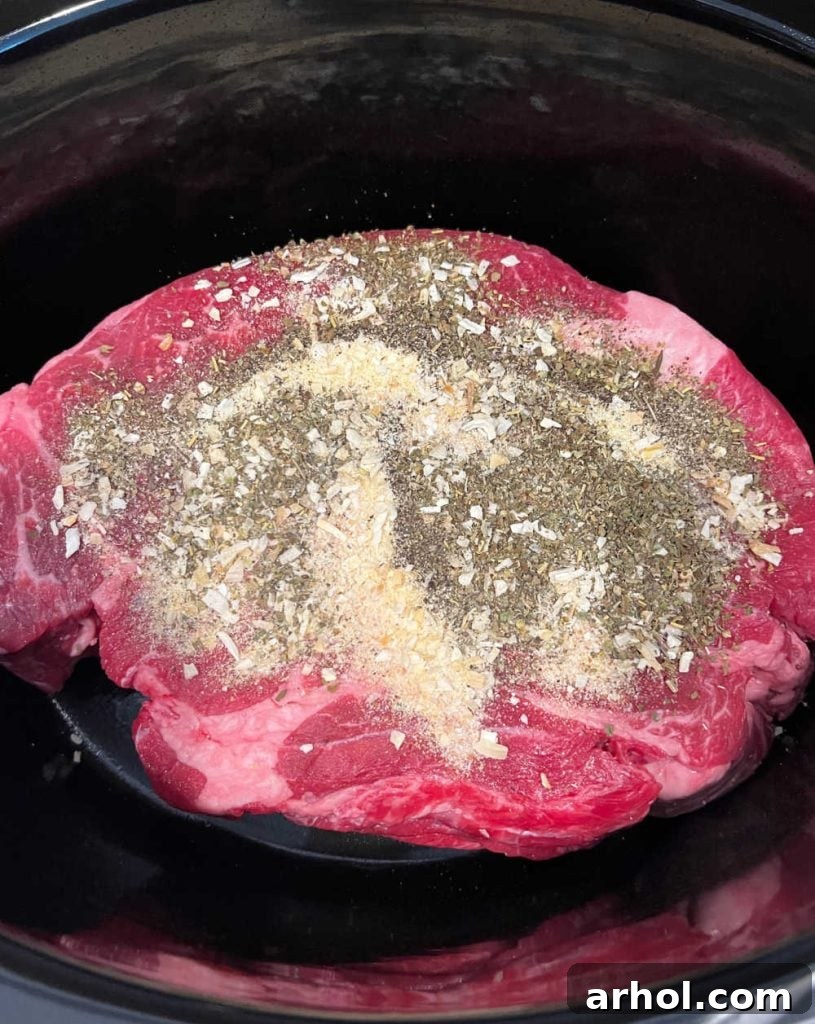 chuck roast seasoned and placed in a slow cooker, ready for additional ingredients.