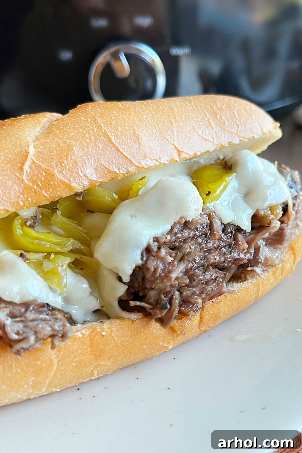 Italian beef sandwich with melted cheese on a plate, garnished with more pepperoncini.