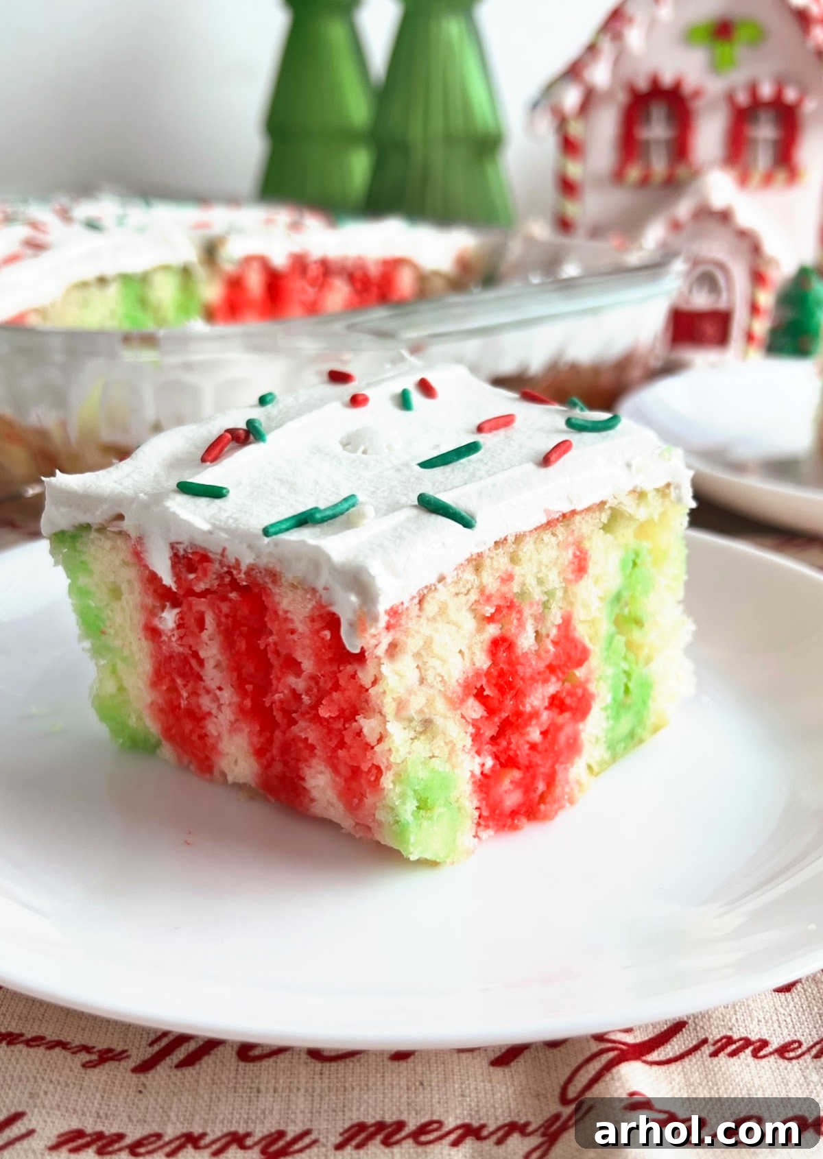Christmas Jello Poke Cake with cool whip frosting and holiday sprinkles on a serving plate.