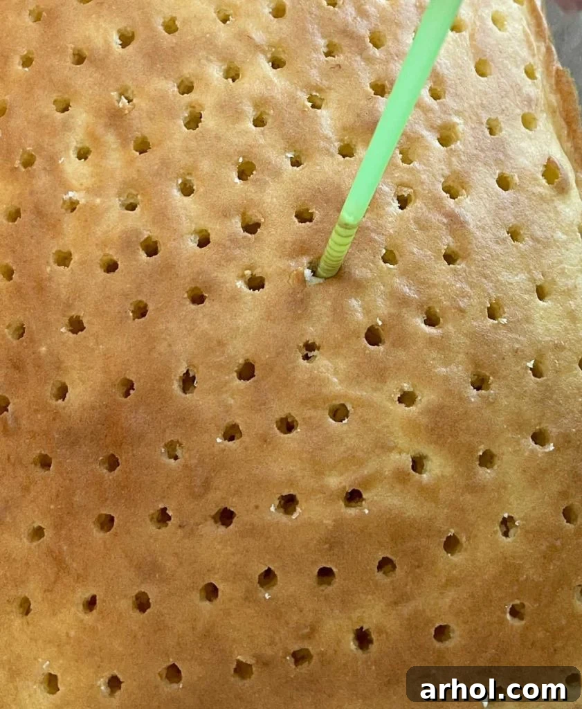 Using a straw to poke holes evenly across the cooled cake.