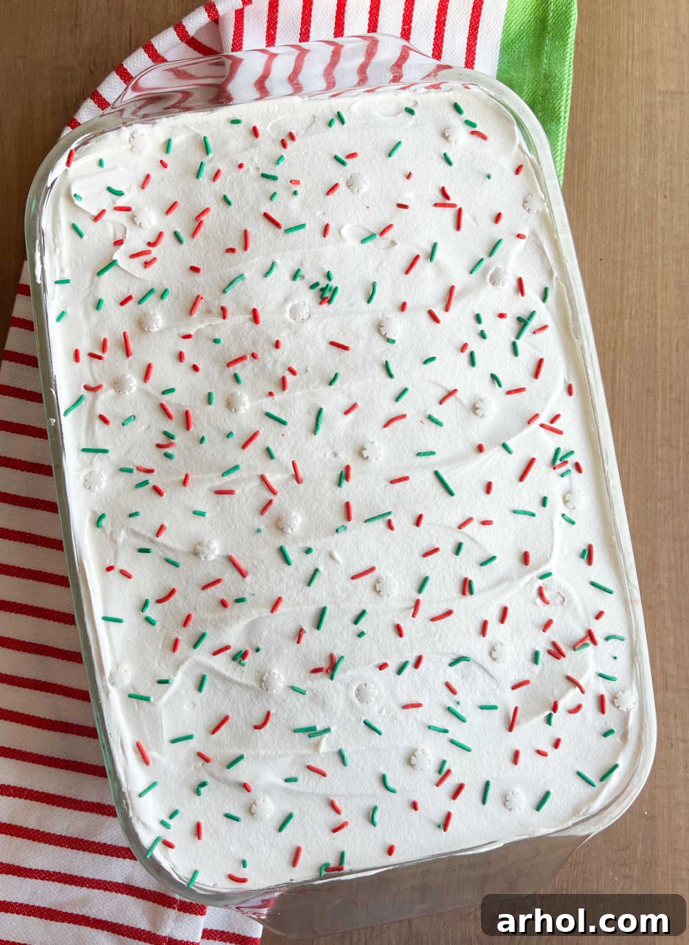 Finished Christmas poke cake with cool whip frosting and red and green sprinkles in a baking dish.