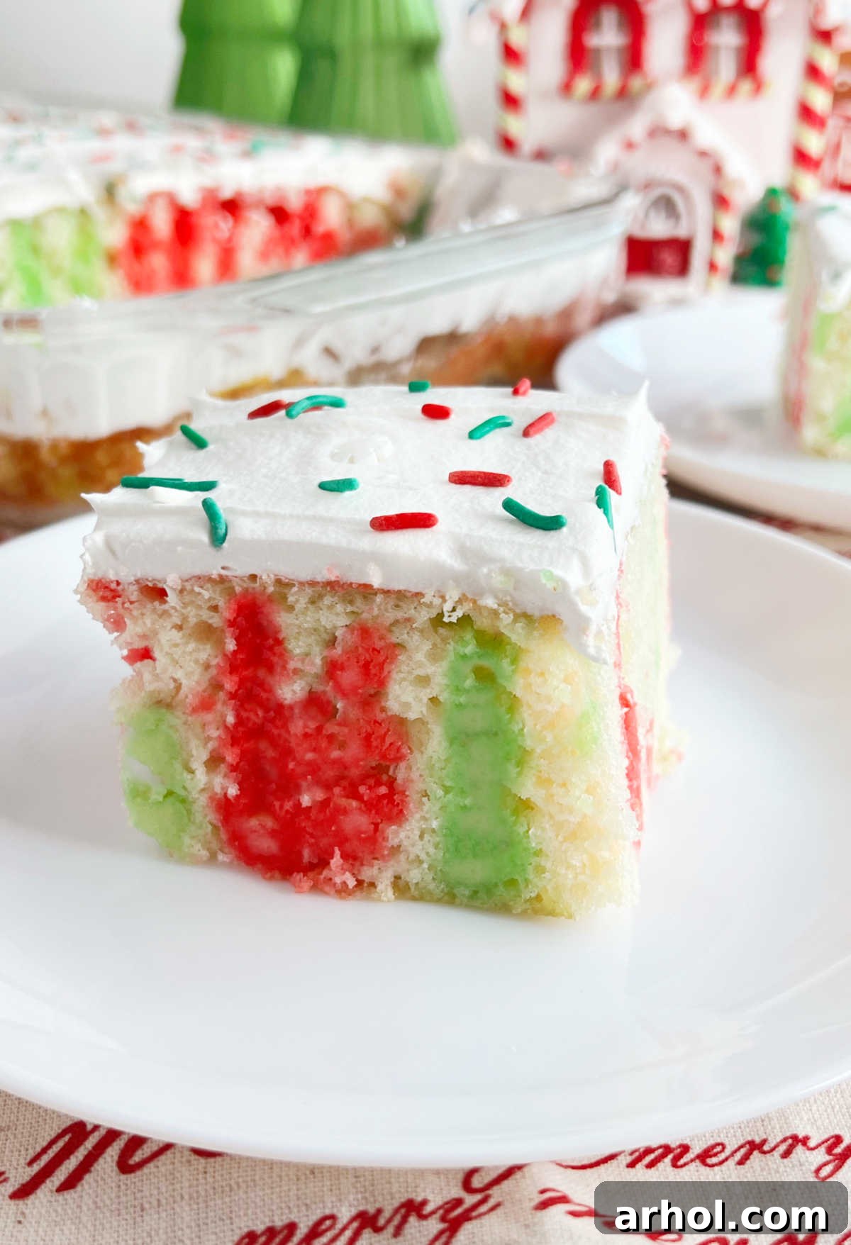 A perfectly sliced piece of Christmas poke cake on a white plate, showing the red and green Jell-O layers.