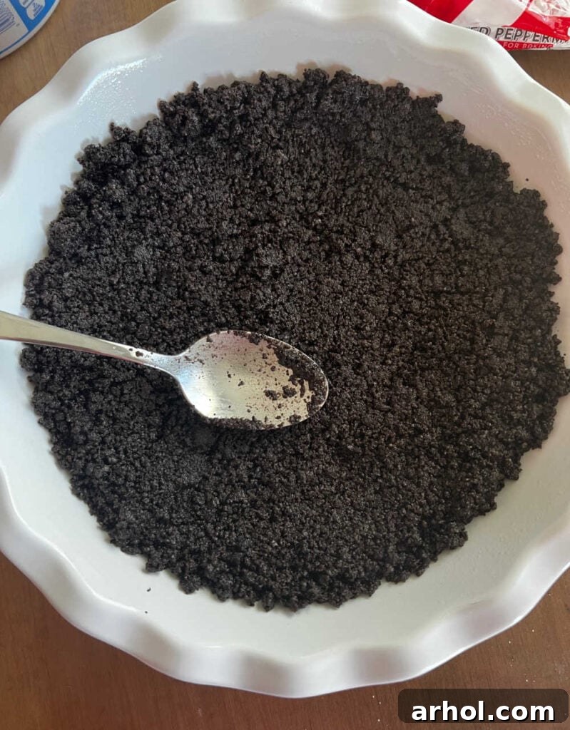 A close-up shot of crushed Oreo cookies being pressed into a pie pan to form the crust.
