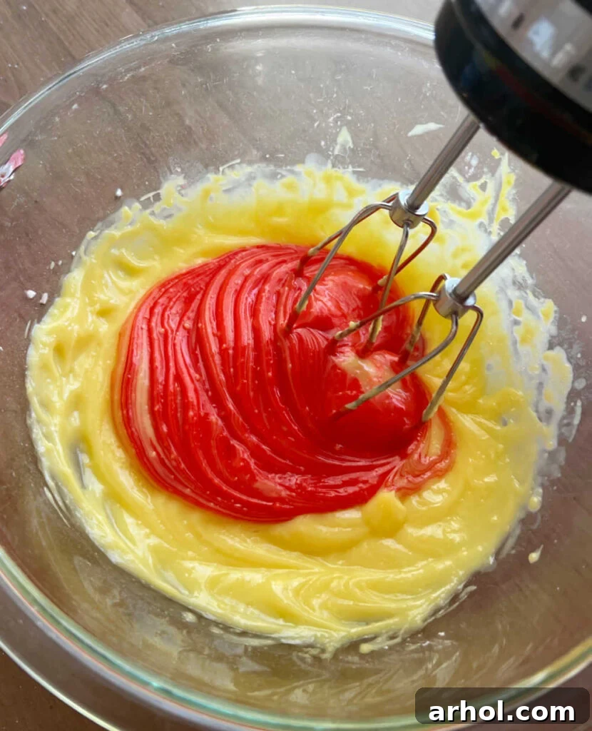 A mixing bowl where instant pudding mix, milk, and red food coloring are being combined with an electric mixer.