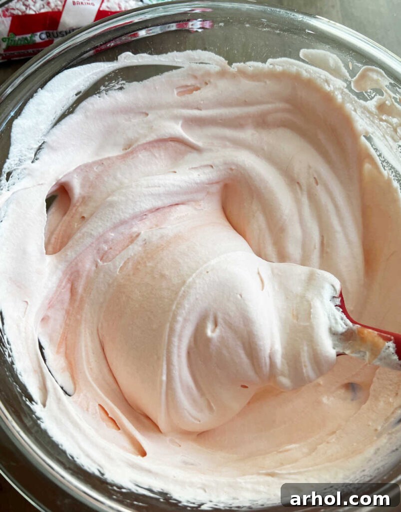 A spatula gently folding whipped topping into a pink pudding mixture in a large mixing bowl.