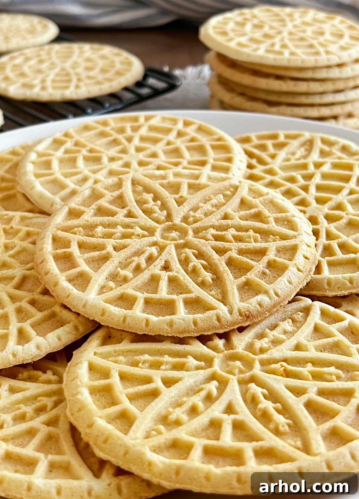 Stacks of homemade pizzelle cookies with flower design on the table, dusted with powdered sugar.
