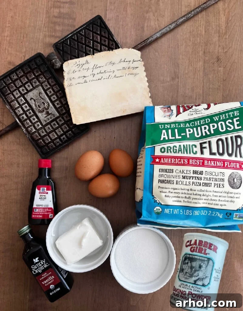 Vintage pizzelle iron alongside ingredients like flour, eggs, anise extract, vanilla extract, shortening, sugar, and baking powder, laid out on a wooden table.