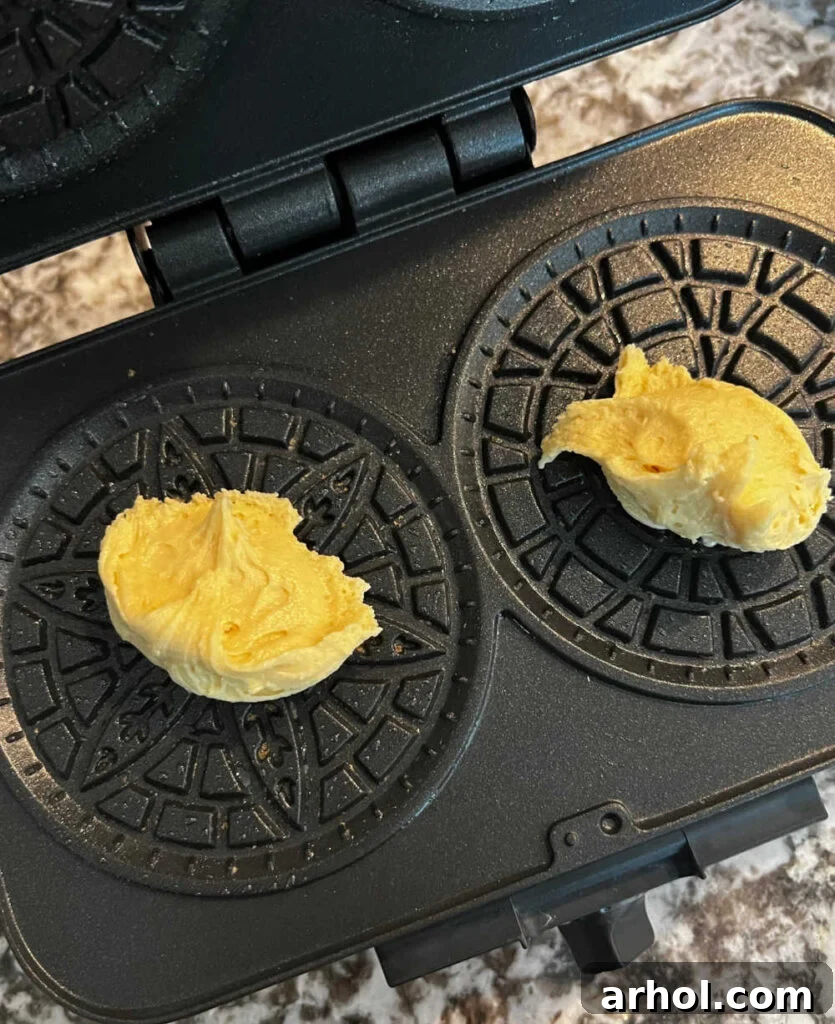 Small balls of pizzelle batter placed onto the hot grids of a pizzelle iron, ready for pressing.