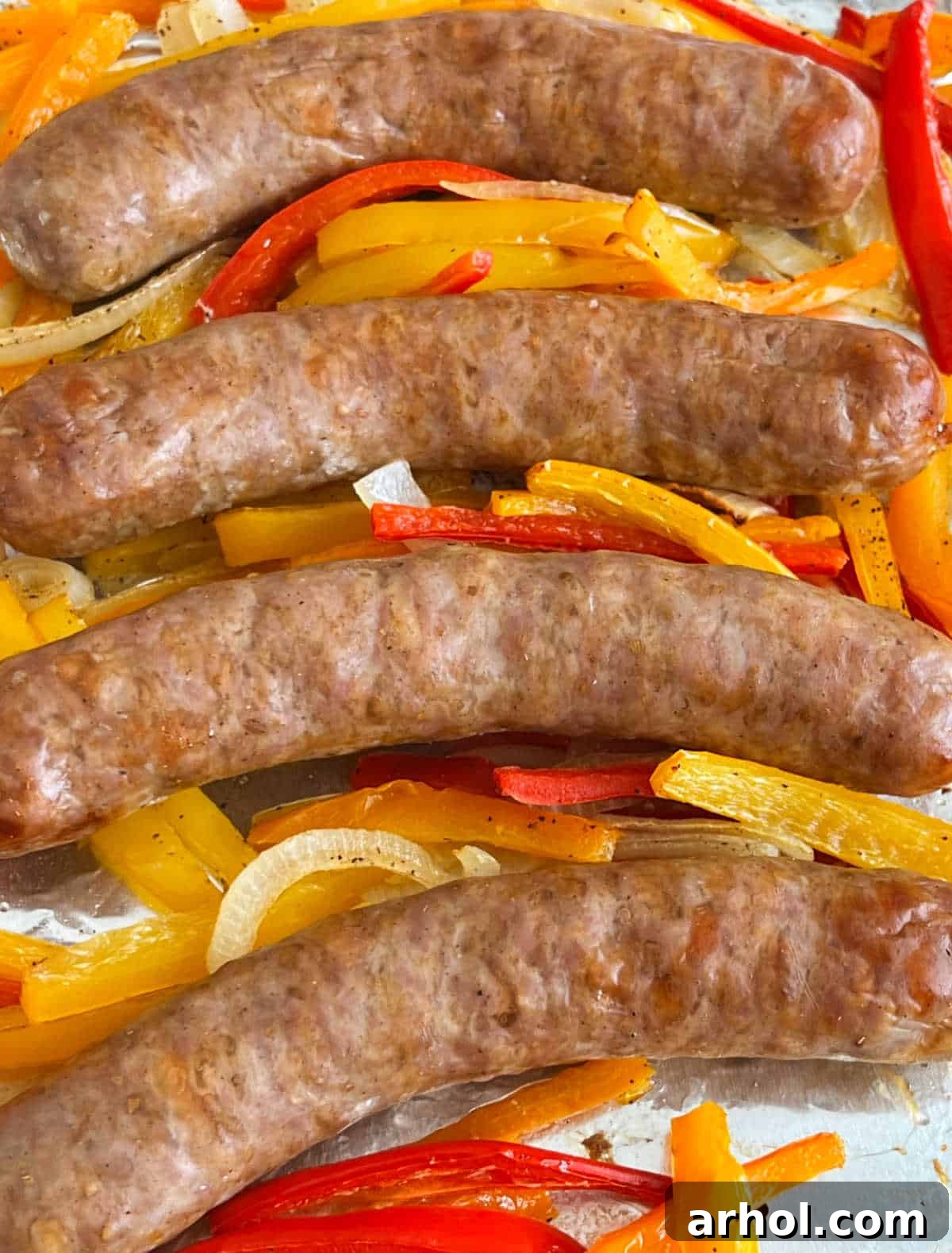 A vibrant, close-up shot of baked sausage, colorful bell peppers, and caramelized onions on a sheet pan, ready to be served.