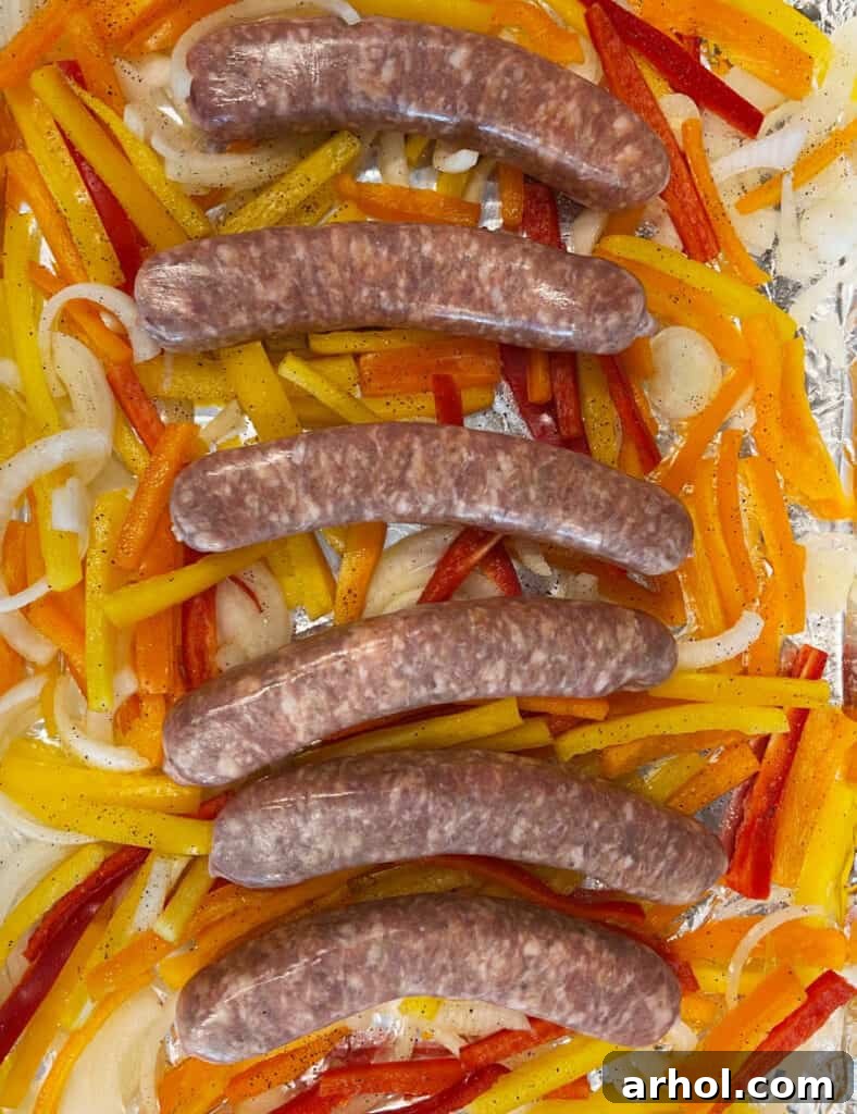 Italian sausages placed on top of a bed of sliced onions and bell peppers on a baking sheet, ready for baking.