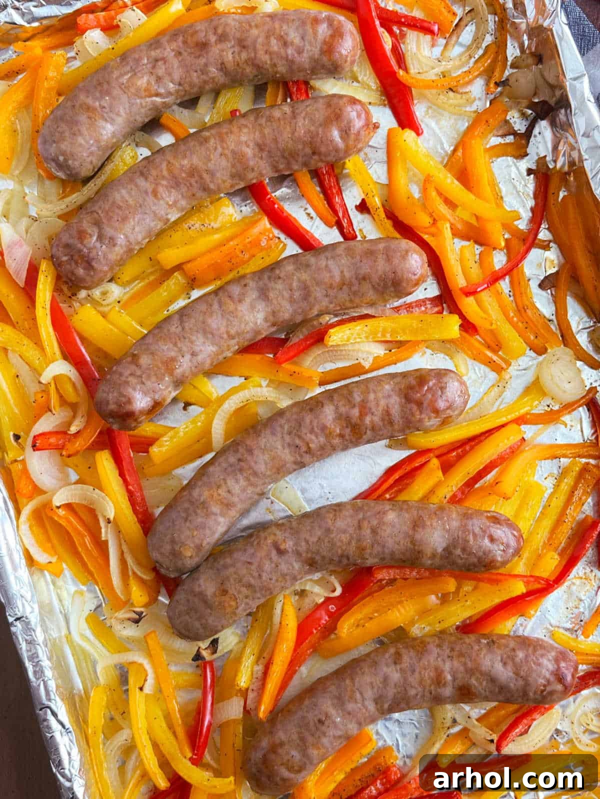 A serving of baked sheet pan sausage, peppers, and onions in a hoagie roll with melted provolone cheese, ready to be enjoyed.