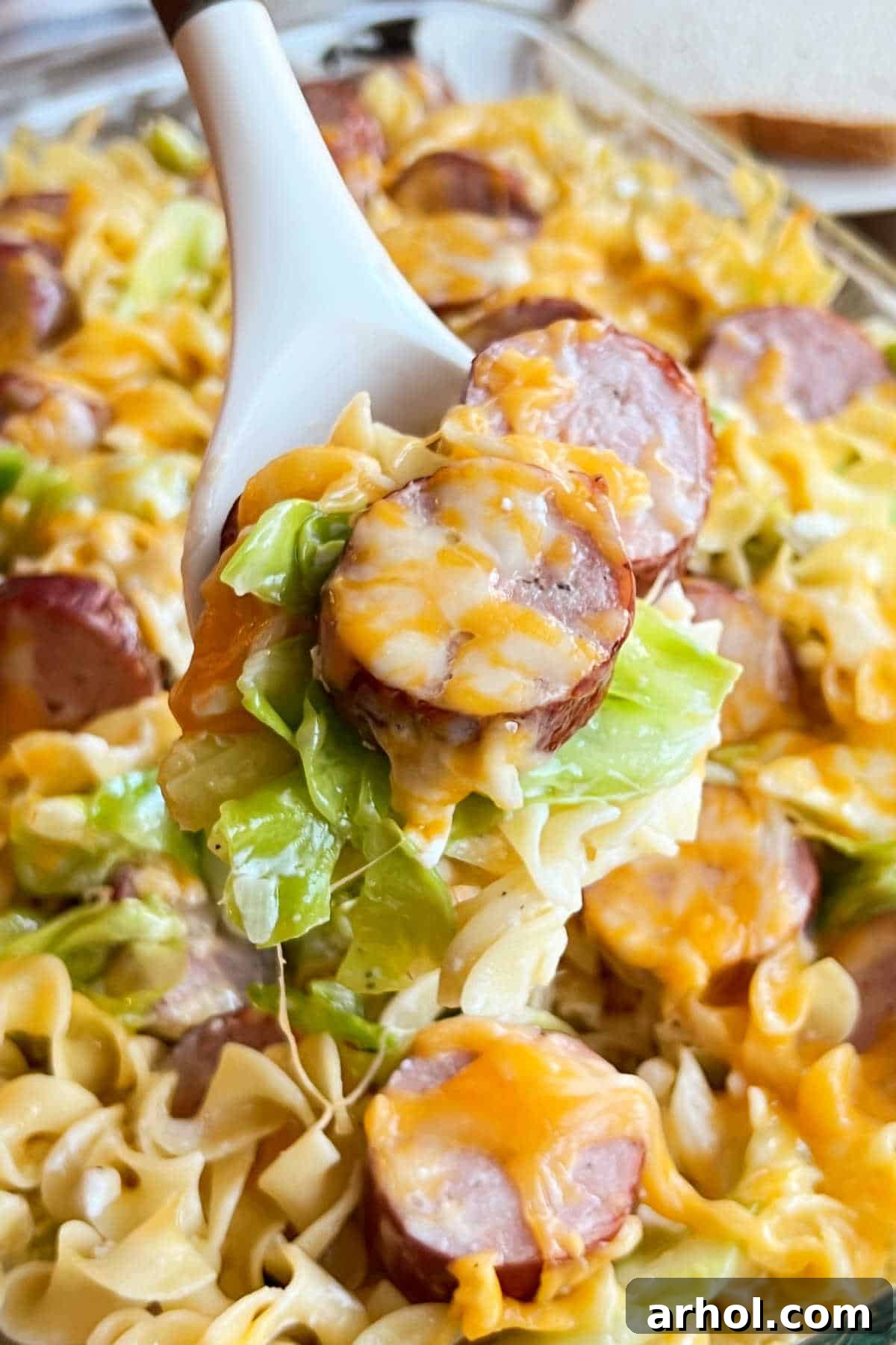 A close-up of a spoonful of cheesy kielbasa casserole with smoked sausage and noodles.